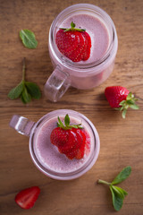 Two glasses of pink strawberry milkshake or cocktail. Strawberry banana smoothie on wooden table. overhead, vertical