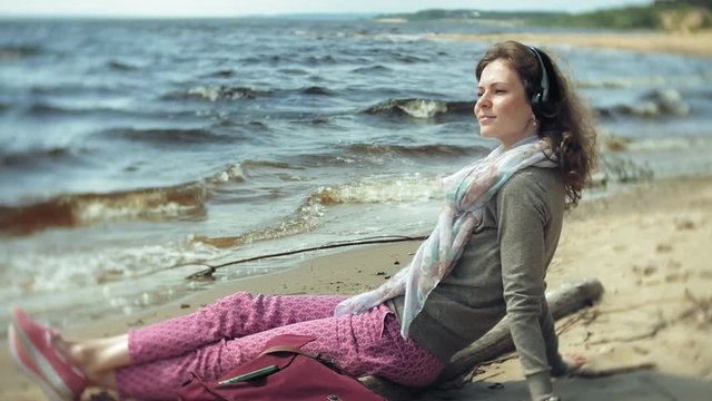 A woman listens to music on headphones, relaxes and dances on the shore of the sea river of the ocean. Technology in the open air
