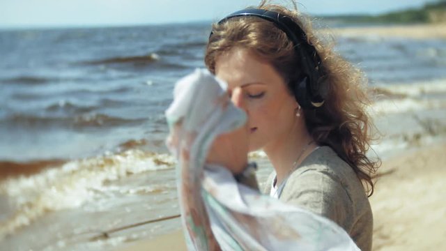 A woman listens to music on headphones, relaxes and dances on the shore of the sea river of the ocean. Technology in the open air