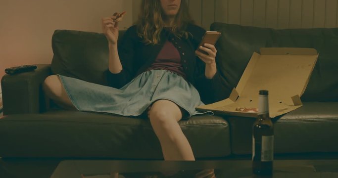 Young woman eating pizza and using smartphone