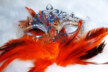 beautiful filigrane ornamental silver venice mask with radiant feathers on white fur structure.