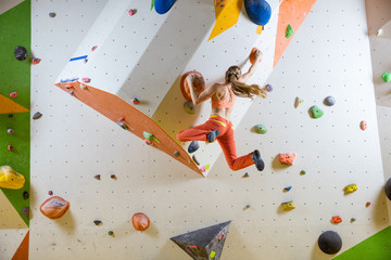 Young woman jumping on handhold in bouldering gym - obrazy, fototapety, plakaty