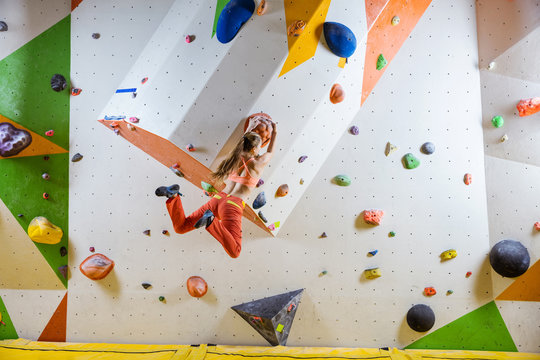 Young athletic woman jumping on climbing hold in bouldering gym