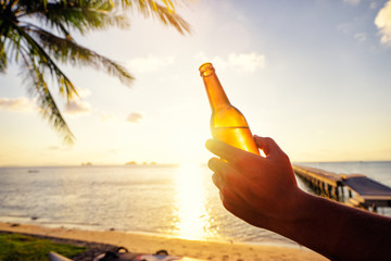 Vacation concept. Male hand holding bottle of beer on the sea beach.