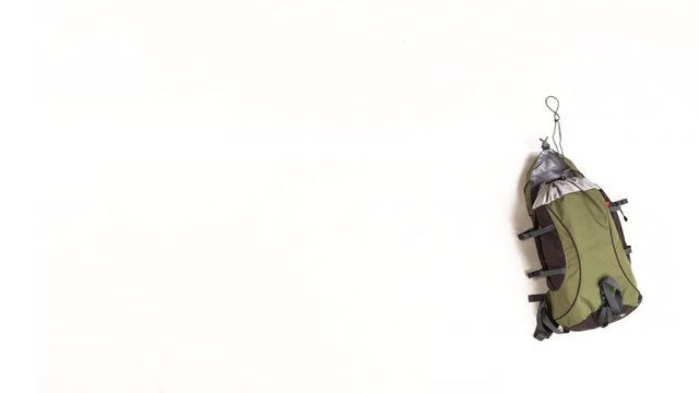Top view on backpack with camping equipment, accessories and hiking clothes on white background. Camping, preparing for expedition and travelling concept. 4k stop motion animation.