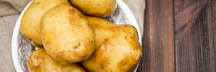 Raw potatoes on a brown wooden background banner