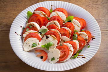 Caprese salad with tomatoes, mozzarella cheese, basil, olive oil and balsamic vinegar on white plate. horizontal