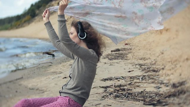 A woman listens to music on headphones, relaxes and dances on the shore of the sea river of the ocean. Technology in the open air