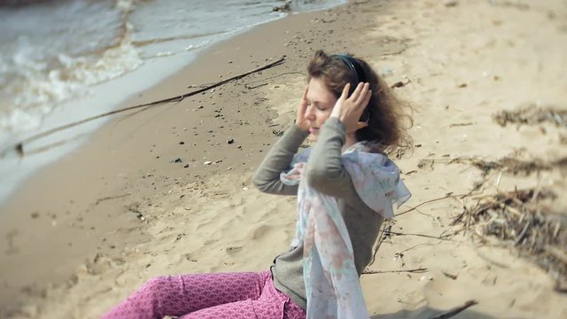 A woman listens to music on headphones, relaxes and dances on the shore of the sea river of the ocean. Technology in the open air