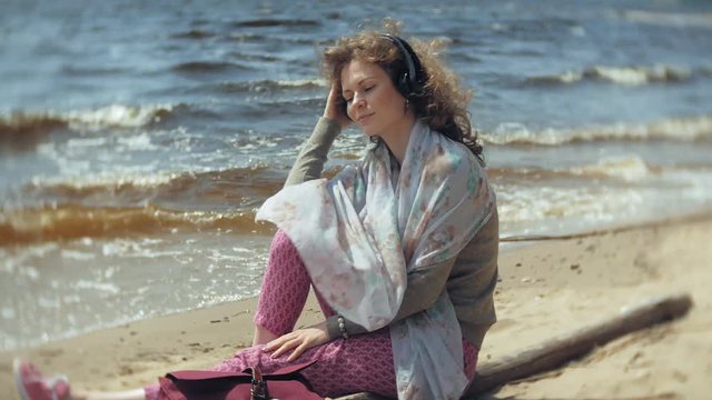 A woman listens to music on headphones, relaxes and dances on the shore of the sea river of the ocean. Technology in the open air