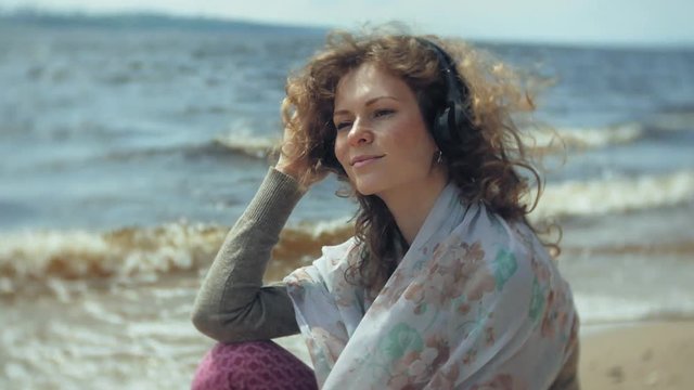 A woman listens to music on headphones, relaxes and dances on the shore of the sea river of the ocean. Technology in the open air
