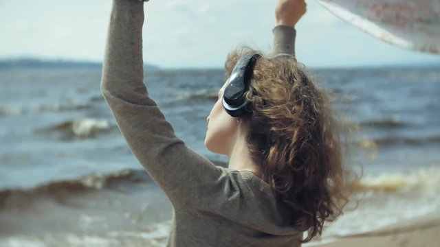 A woman listens to music on headphones, relaxes and dances on the shore of the sea river of the ocean. Technology in the open air