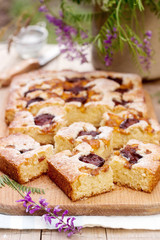 Pieces of fruit pie with pieces of plums and peach and a bouquet of flowers on a wooden table. Rustic style.