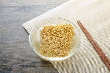 Glass bowl , chopsticks and instant noodle on the wooden table.