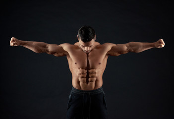Naklejka premium Frontview of strong sportsman demonstrating arm muscles. Man having clear body reliefs , healthy, athletic figure. Sport lifestyle. Regular gym trainings. Fit sporty body. Bllack studio background.