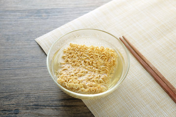 Glass bowl , chopsticks and instant noodle on the wooden table.