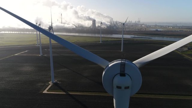 Aerial moving through wind turbine blades located at solar park in background showing some heavy industry and nuclear power plant showing the exhaust fumes emerging from the cooling towers 4k quality