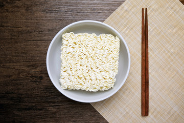 Top view of instant noodle in the glass bowl near the chopsticks on the wooden table.