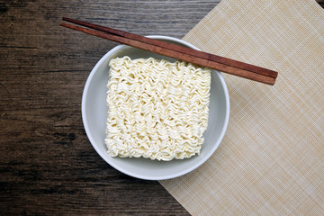 Top view of instant noodle in the glass bowl near the chopsticks on the wooden table.