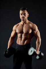 Fototapeta na wymiar Attractive, handsome man holding heavy dumbbells. Athlete having strong, healthy, fit body with clear muscular relief and powerful hands. Looking sexy. Sport lifestyle. Feeling confident.
