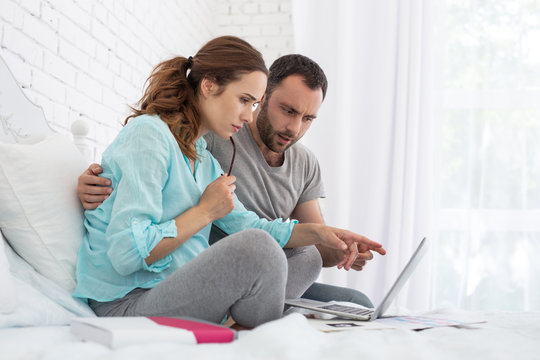 Online magazine. Attractive pregnant woman and man using laptop and sitting on bed