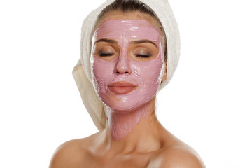 young smiling woman posing facial mask on her face with a towel on her head