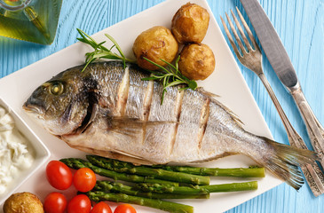 Baked dorado fish with potatoes, asparagus and tomatoes.