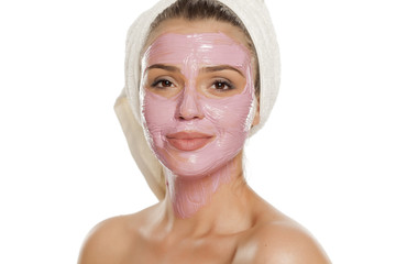 young smiling woman posing facial mask on her face with a towel on her head
