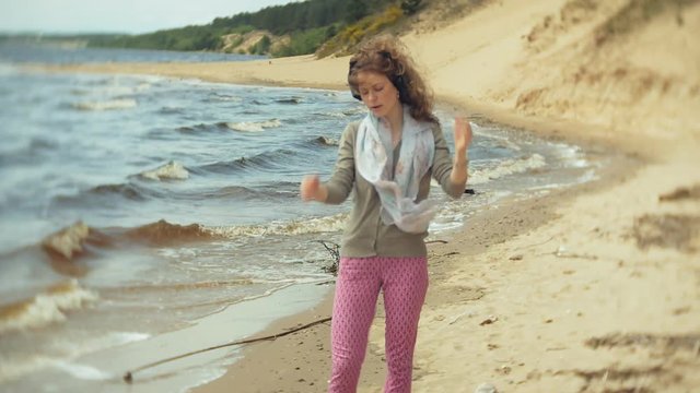 A woman listens to music on headphones, relaxes and dances on the shore of the sea river of the ocean. Technology in the open air
