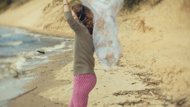 A woman listens to music on headphones, relaxes and dances on the shore of the sea river of the ocean. Technology in the open air