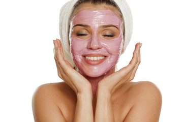 young smiling woman posing facial mask on her face with a towel on her head