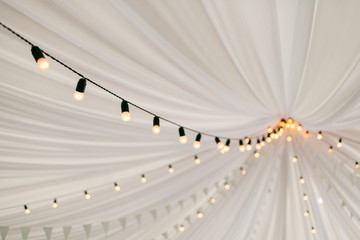 Garlands of lamps on a cord in a white tent. A wedding Banquet.