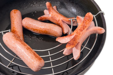 Fried vienna sausages on lattice in frying pan closeup