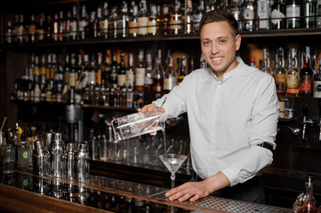 Smiling bartender adding an alcoholic drink into the martini glass