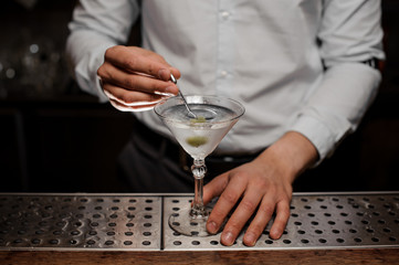 Bartender adding an olive on the skewer into the martini glass