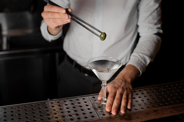 Bartender adding an olive into the martini glass with tweezers