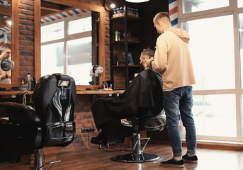 Fototapeta na wymiar Professional barber working with client in hairdressing salon