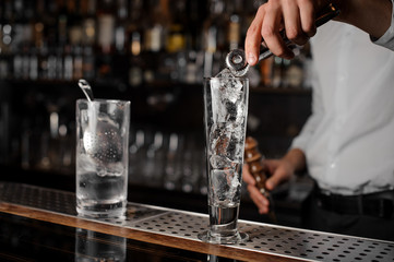 Bartender adding ice cubes into an empty cocktail glass