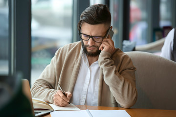 Young freelancer with mobile phone working in cafe