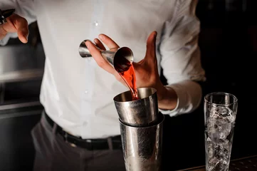 Tuinposter Professional bartender adding a transparent red alcoholic drink into the steel shaker © fesenko