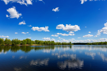 Naklejka na ściany i meble Beautiful summer landscape of river view with blue cloudy sky and wild forest reflections in water.