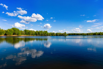 Beautiful summer landscape of river view with blue cloudy sky and wild forest reflections in water.