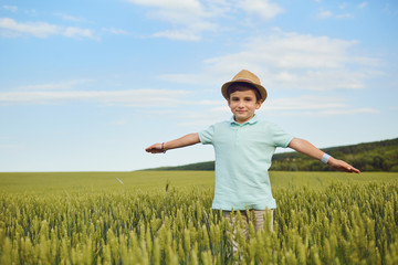 A happy boy in a hat smiles in a field of wheat in the summer.