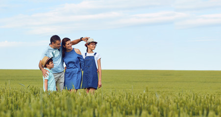 A happy family standing in a wheat field in summer points to a place for text.