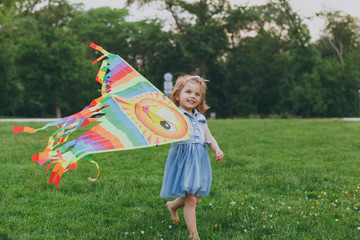 Smiling little cute child baby girl in denim dress walking, play with colorful kite and have fun in green park. Mother, little kid daughter. Mother's Day, love family, parenthood, childhood concept.