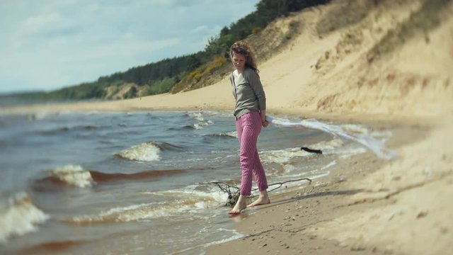 A woman listens to music on headphones, relaxes and dances on the shore of the sea river of the ocean. Technology in the open air