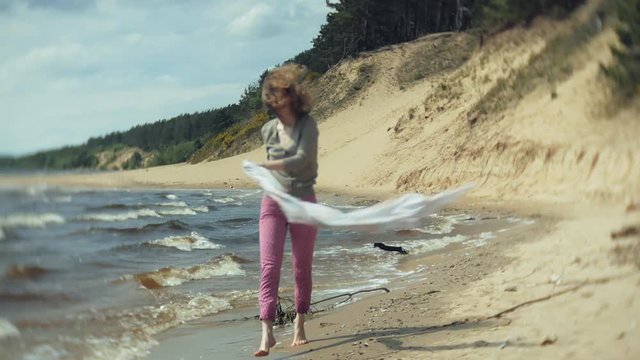 A woman listens to music on headphones, relaxes and dances on the shore of the sea river of the ocean. Technology in the open air