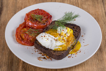 Poached egg on a piece of bread with fried red tomatoes, close up