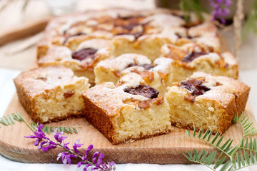 Pieces of fruit pie with pieces of plums and peach and a bouquet of flowers on a wooden table. Rustic style.