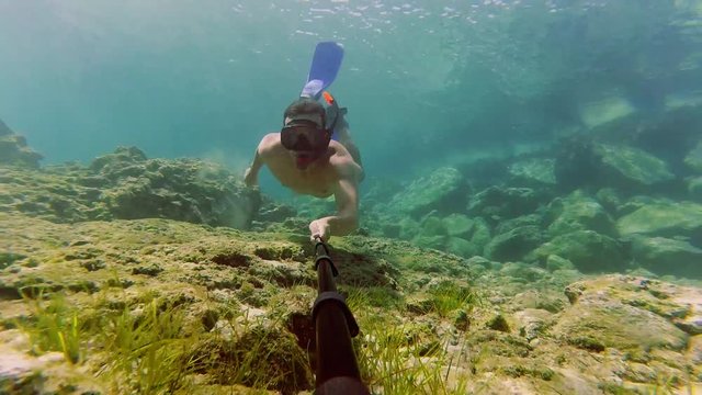 Young man dives with snorkel and shooting underwater video